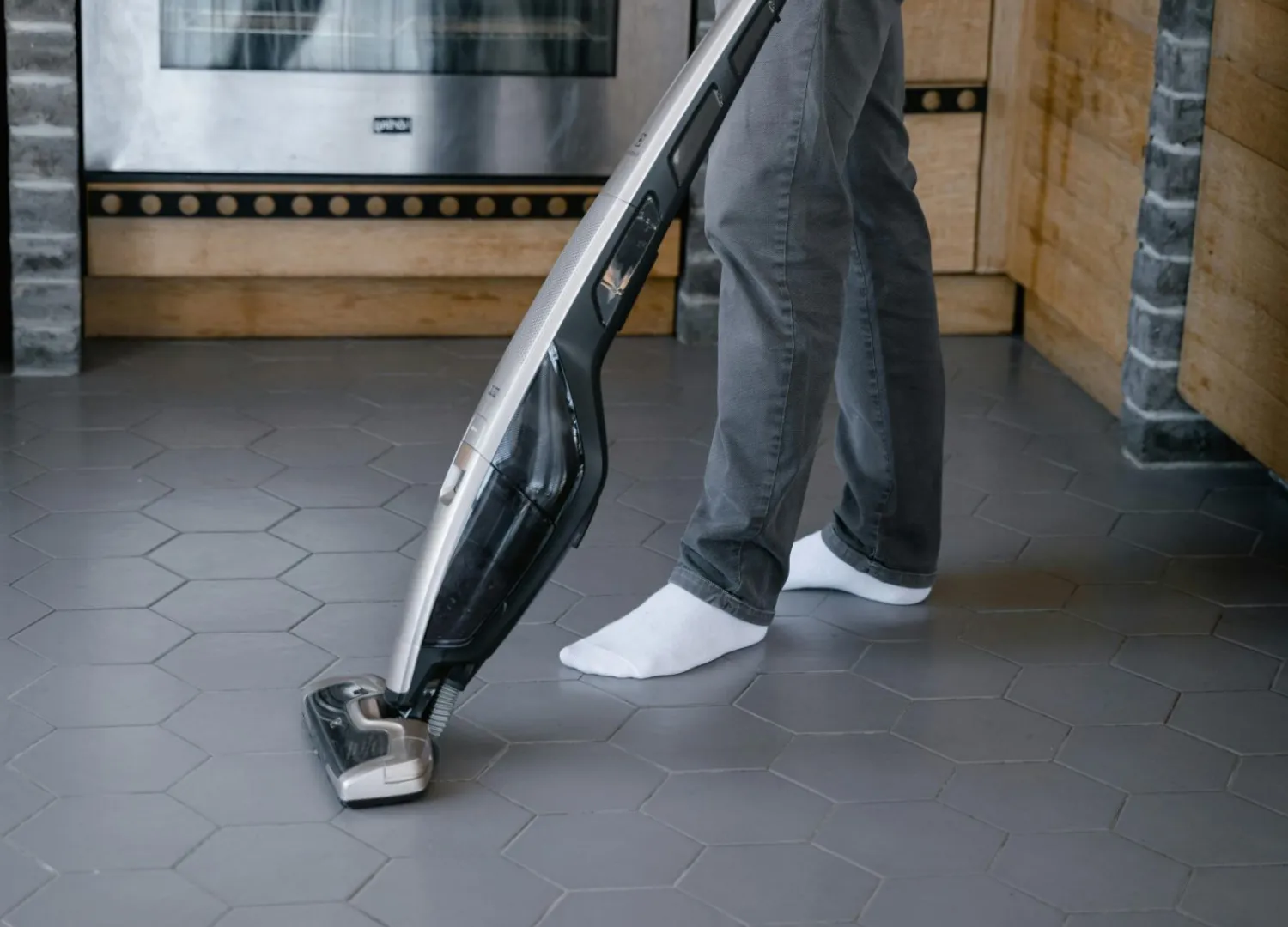 Pessoa usando um aspirador de pó em uma cozinha com piso de porcelanato.
